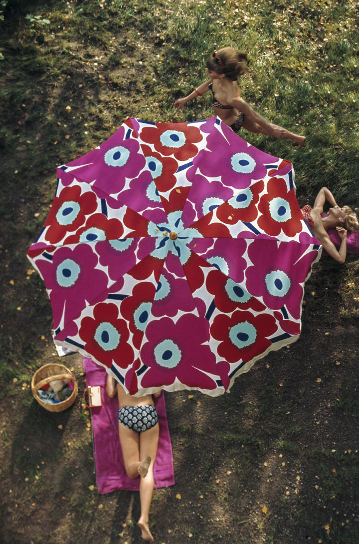 Een afbeelding van een Unikko parasol van bovenaf met een vrouw in de zon eronder.
